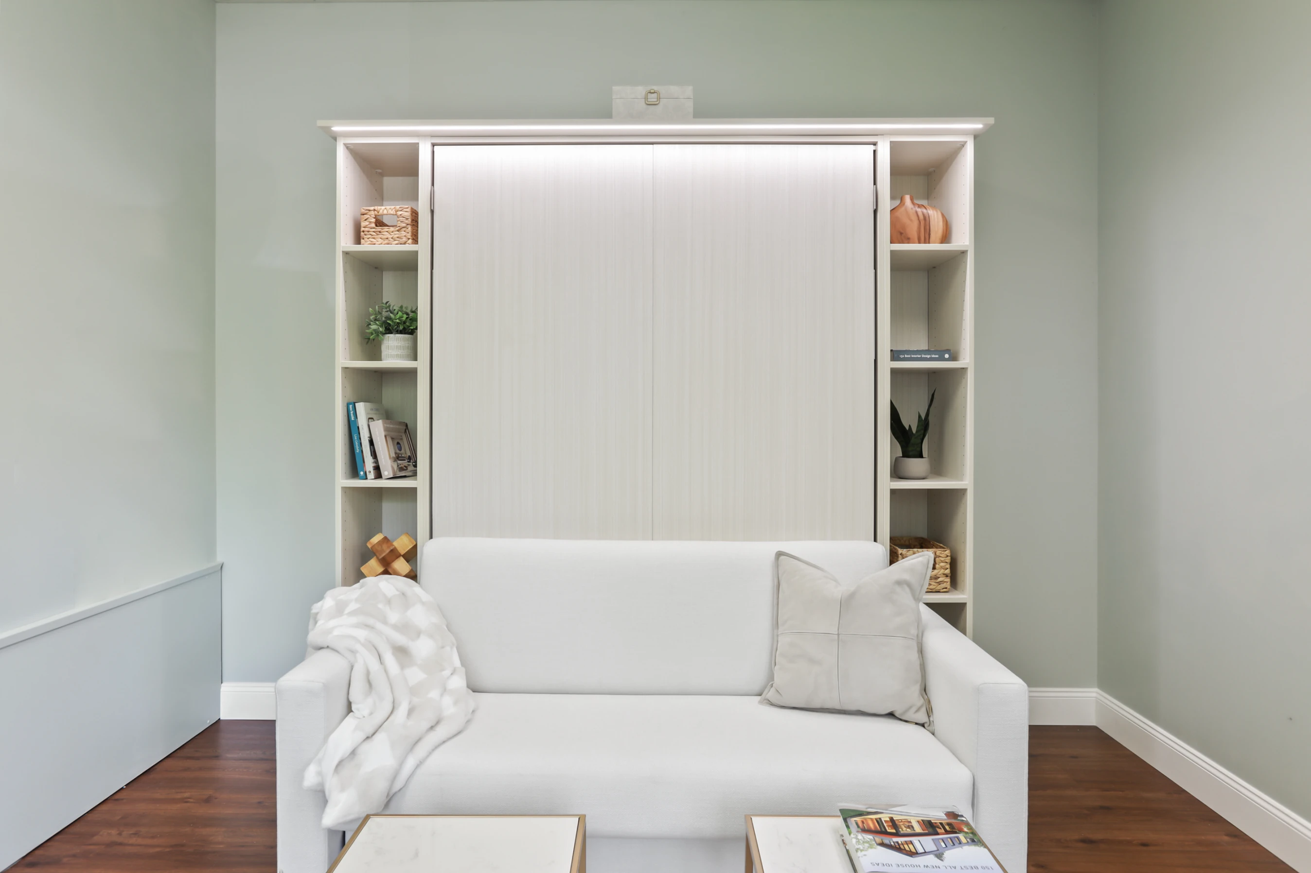Murphy Bed with a blue couch and custom shelving, in white finish. Built by Bella Systems NJ